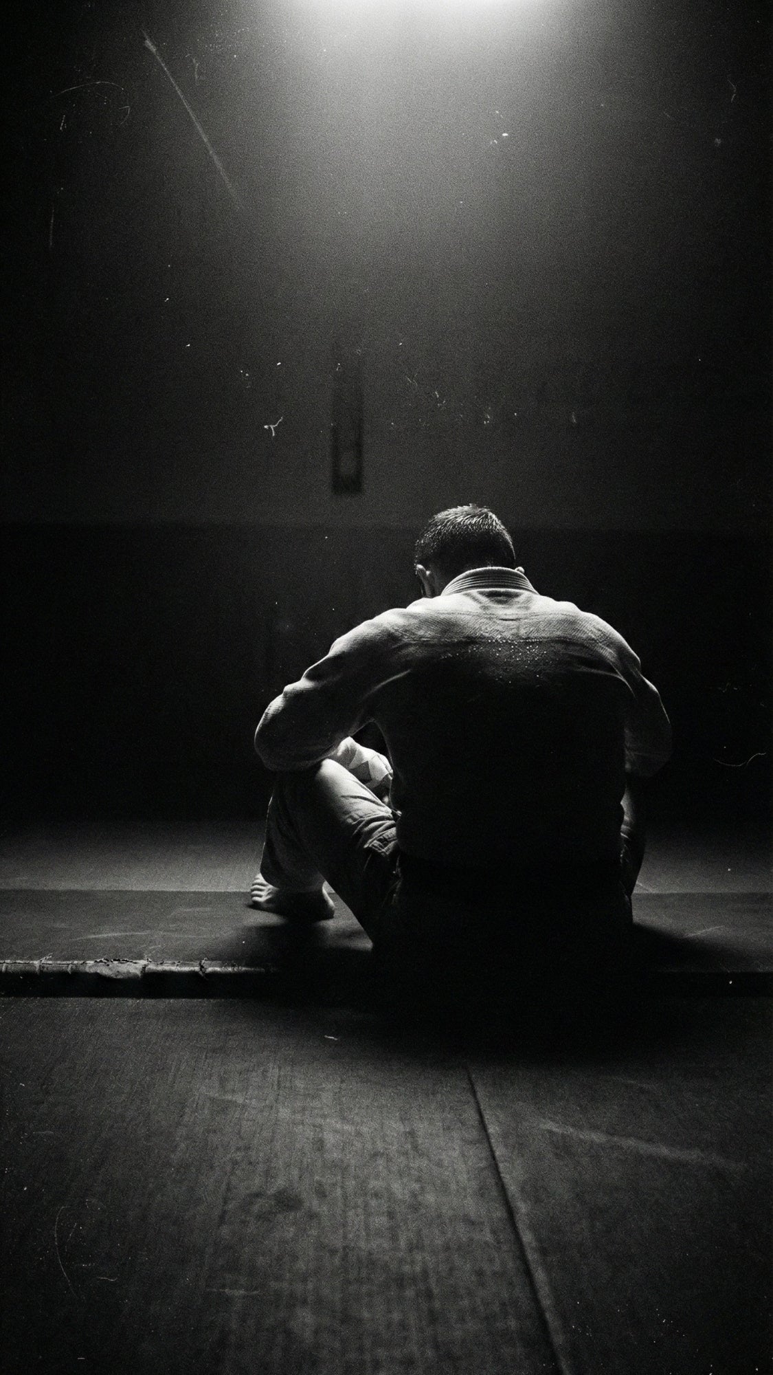 Mobile Header: BJJ Athlet im Gi sitzt fokussiert auf der Matte. Vertikale Schwarz-Weiß Ästhetik visualisiert das Mat Defense Mindset auf dem Smartphone.
