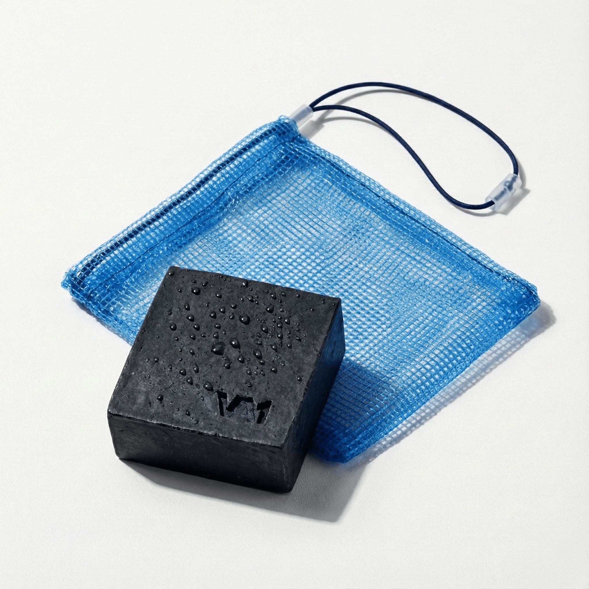 Nahaufnahme der nassen VA1 Core Bar Aktivkohle Seife mit Logo und Wassertropfen vor dem Seifenbeutel. Detailansicht der Textur für spezialisierte Matten-Hygiene.