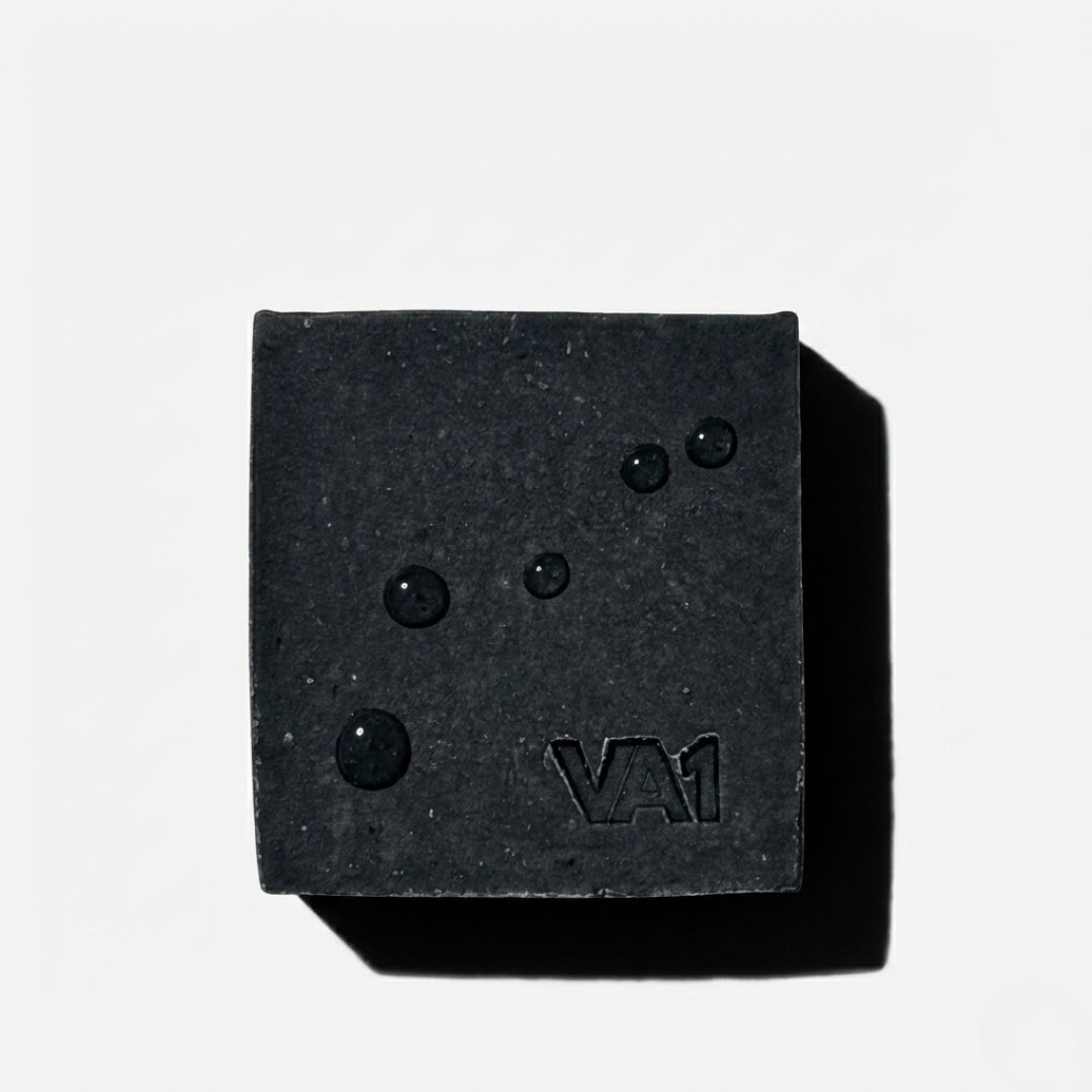 Minimalistische Draufsicht der VA1 Core Bar mit einzelnen Wassertropfen. Clean Product Shot der Aktivkohle-Seife mit sichtbarem Logo.