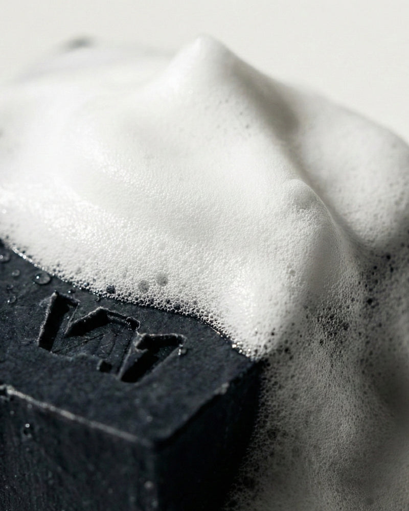 Nahaufnahme der schäumenden VA1 Core Bar mit Logo. Intensiver Aktivkohle-Schaum für tiefe Porenreinigung und Mat Defense Hygiene nach dem Training.