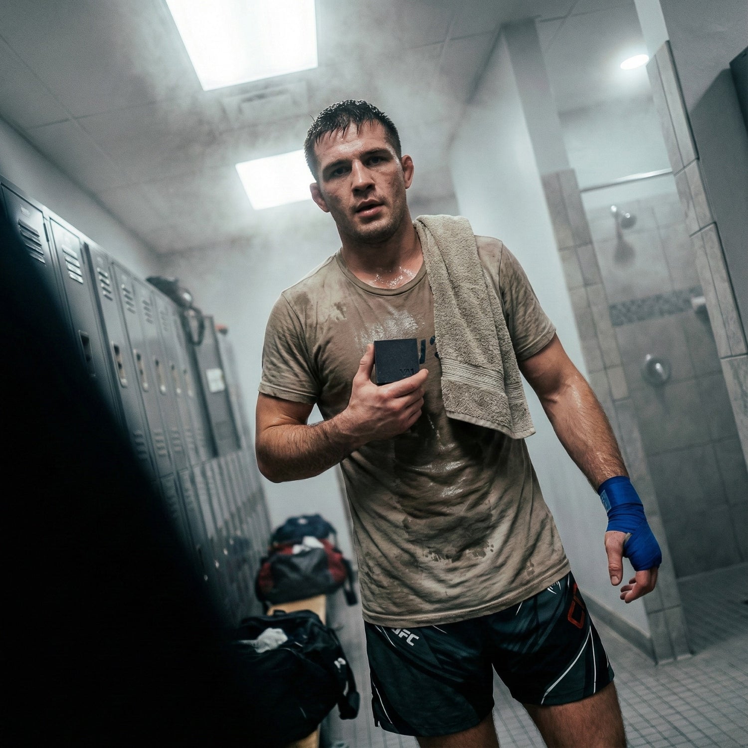 Erschöpfter Athlet im verschwitzten Shirt hält die VA1 Core Bar. Post-Workout Hygiene Routine für Ringer und Grappler im Umkleideraum.