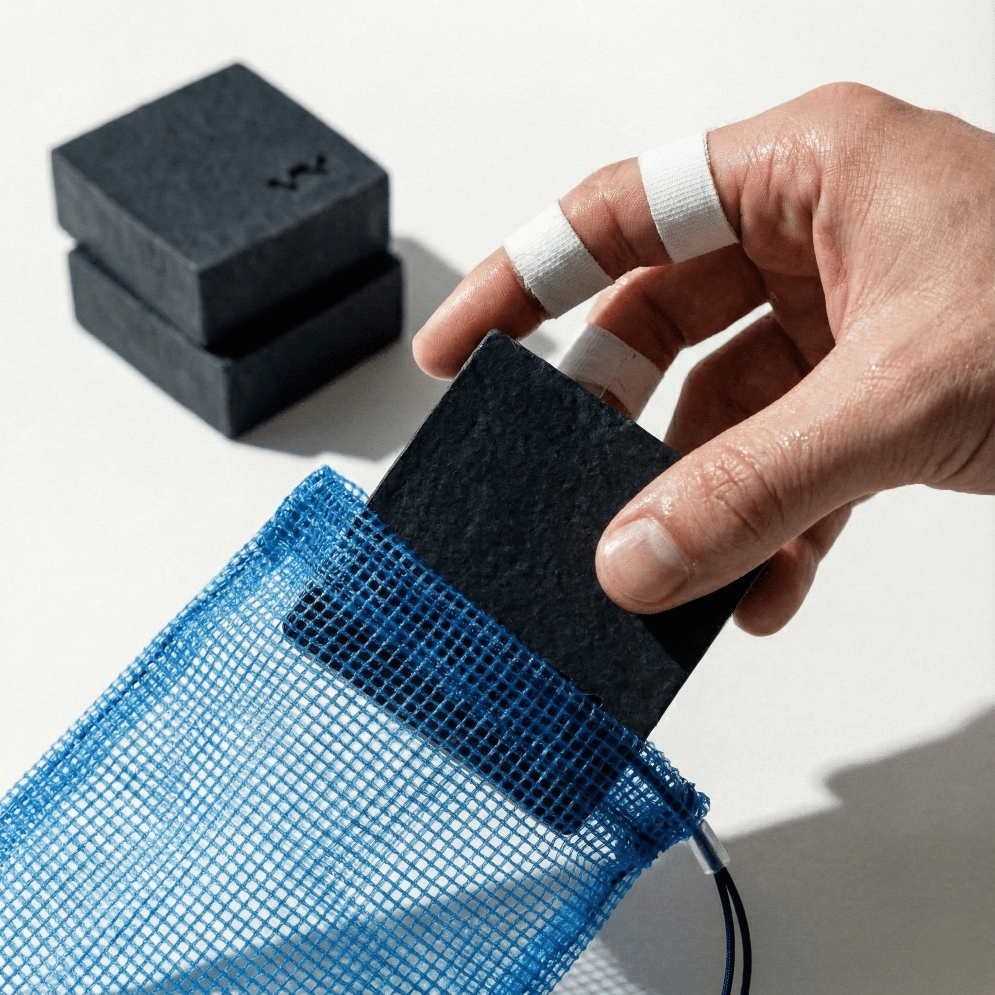 Grappling-Hand mit Finger-Tape beim Einlegen der VA1 Core Bar in den Seifenbeutel. Vorbereitung der Mat Defense Hygiene-Ausrüstung für das Training.